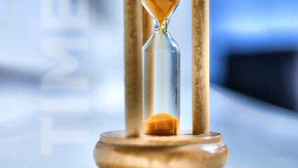 Close-up of a beautiful wooden hourglass with orange sand pouring inside