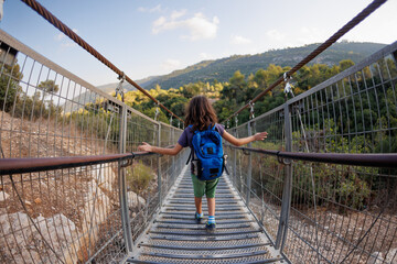 hiking with children. rear view. a boy with a backpack crosses the canyon through a rope bridge. traveling with children.