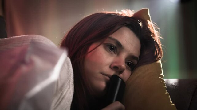 Portrait of a thoughtful red-haired woman who indifferently switches TV channels and does not watch them