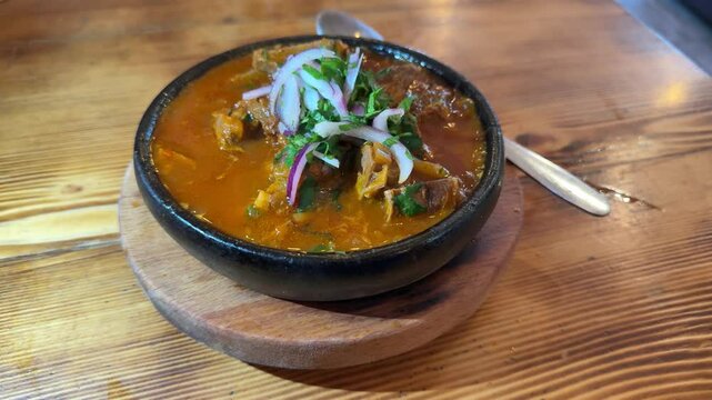 Slow motion view of Ostri, traditional Georgian stew served in rustic clay bowl. Bubbling dish is garnished with fresh herbs and onions, emphasizing its authentic appeal. Bowling Ostri from stove