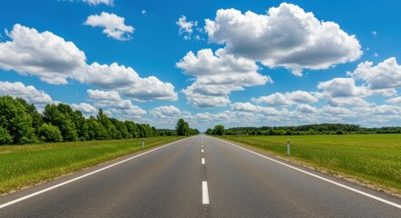 Fototapeta premium A long asphalt road stretching into the distance under a bright blue sky with fluffy white clouds