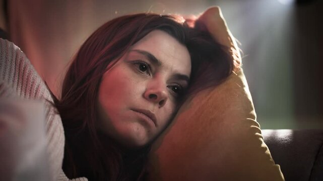 Portrait of a beautiful red-haired woman who eats potato chips. She indifference switches TV channels and does not watch them