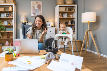 Young woman, mother and business woman, sitting at home online shopping with credit card on laptop...