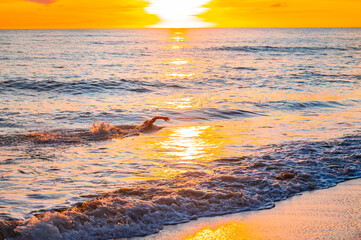 Silhouette of a swimmer in the last orange rays of the setting sun, the swimmer enjoys swimming by...