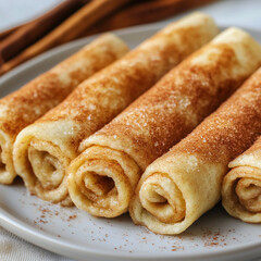 Golden cinnamon sugar crepes rolled into spirals on a white plate