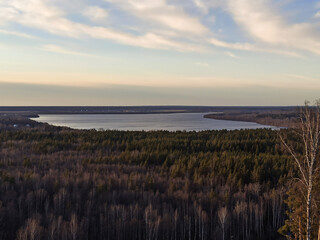 A beautiful soothing view from a height of open spaces, forests and a blue lake in the evening against the background of a cloudy sunset sky in spring in the Leningrad Region.