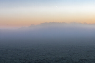 Obraz premium Sunrise over the rolling hills of the sint Pietersberg in Maastricht on a misty December morning, creating a fairy like landscape with the sun peaking through the fog