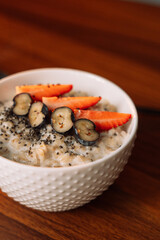 Oatmeal with strawberries in a white bowl on wooden background, vertical photo