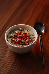 quinoa porridge in a white bowl with pomegranate and nuts, vertical photo
