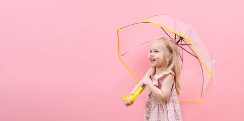 A little child girl holds a transparent umbrella and smiles on a pink isolated background