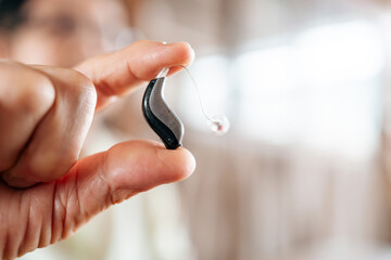 Close-up of a senior hand holding a modern hearing aid device, showcasing advanced technology for...