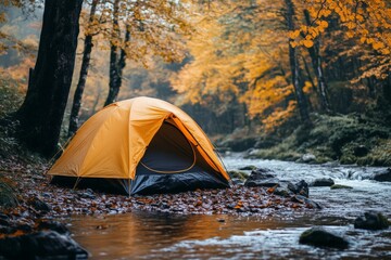 Camping in a vibrant forest with an orange tent near a flowing stream during autumn