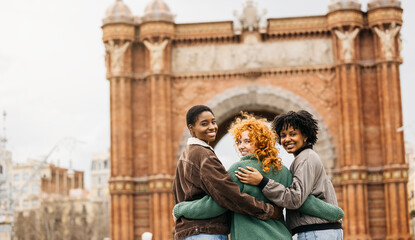 Three female tourists hugging, visiting arc de triomf in barcelona, spain