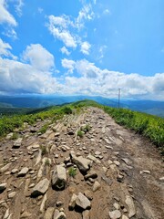 Hiking trail on Połonina Caryńska, Bieszczady, Poland, with grassy meadows and distant mountains under a partly cloudy sky.