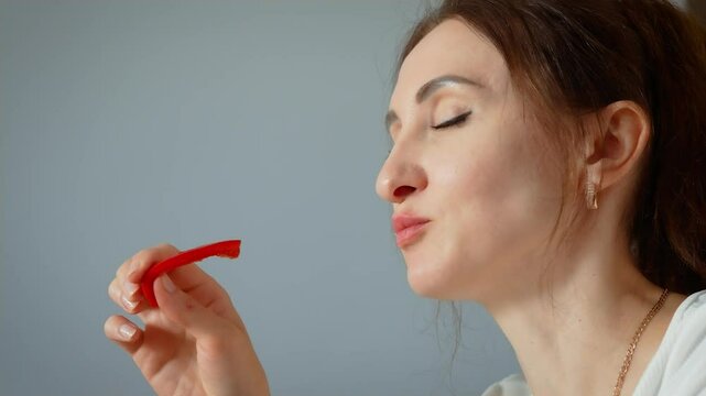 Young woman eating red sweet pepper slice. Female savoring fresh bell pepper with thoughtful expression. Lady enjoying crisp vegetable during relaxed dining moment