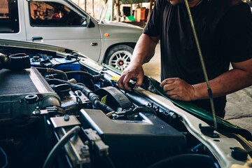 Professional male mechanic works diligently repairing a car in service center. Car radiator coolant...