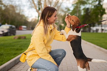 A woman kneels to interact joyfully with her dog while both enjoy a pleasant park walk.