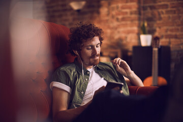 Man relaxing on couch with headphones listening to music and using smartphone