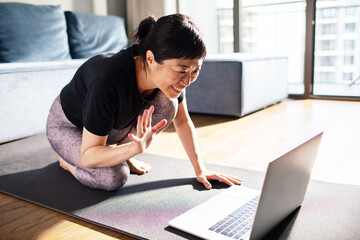 Woman using laptop on yoga mat at home during workout