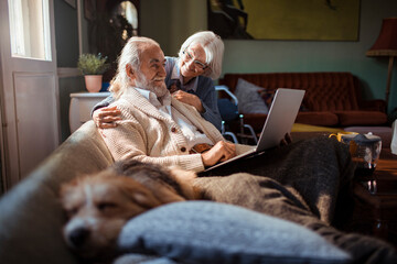 Elderly couple embracing while using laptop at home