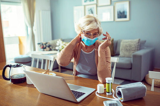 Senior woman wearing face mask taking medication while using laptop at home