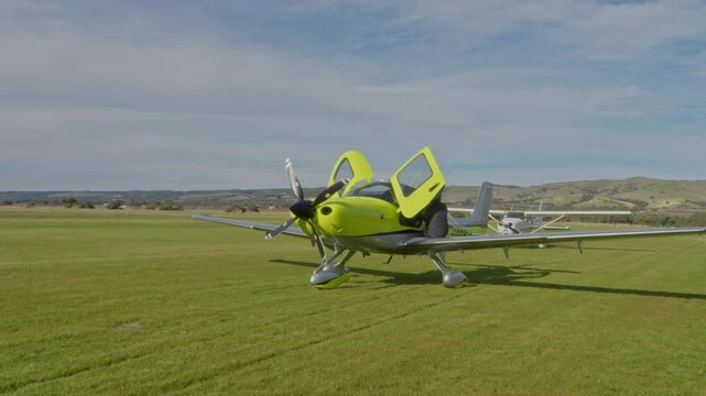 Green JMB VL3 Ultralight Private Aircraft Aviation Parked at Regional Airstrip on Grass Blue Sky Clouds Wide Shot