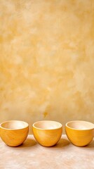 Pale yellow wooden bowls arranged in a row against a textured ochre-yellow wall creating a calming and serene atmosphere