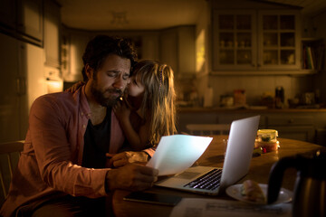 Daughter consoling her father who is worried about the home finances while sitting in the kitchen...