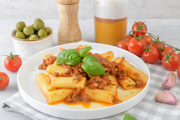 Rigatoni pasta with classic Bolognese sauce served on white plate on light gray background
