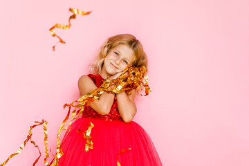 Girl with long hair in festive paper hat and dressy dress on pink background tossing gold confetti