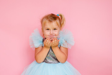 Girl with long hair in festive paper hat and dressy dress on pink background tossing gold confetti