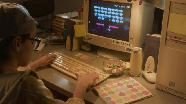 Follow shot of young 90s boy inserting floppy disc into retro computer and playing video games at home