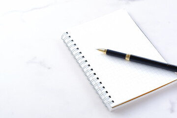 リング式のメモ帳とペンでデスクワークをしているイメージ
