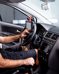 Un t&eacute;cnico automotriz utilizando una herramienta de diagn&oacute;stico montada en el volante dentro del interior moderno de un autom&oacute;vil, realizando pruebas de sistemas del veh&iacute;culo