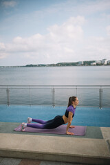 Woman practicing yoga beside a serene waterfront during the day in a peaceful outdoor setting