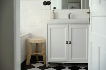 Retro style elegant bathroom interior through open door. Wash basin, cabinet, mirror. Marble soap dispenser. Black white checkered floor white tile wall background. Elegant minimal Scandinavian design