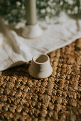 A white candle holder sits on a rug. The candle holder is white and has a small base. The rug is brown and has a pattern