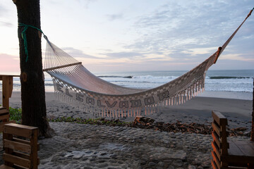 l Salvador on a hammock hanging at the empty beach patio during sunset hour. Selective focus,...
