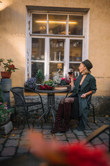 Stylish woman enjoying a drink at an outdoor cafe in a historic setting during sunset