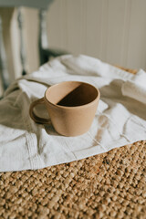 A ceramic coffee cup is placed on a white cloth on a wooden table. The cup is empty and the cloth is made of a soft, woven material. The table is made of wood and has a natural, rustic appearance