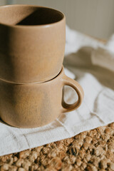 Two cups are sitting on a white cloth, one of which is slightly larger than the other. The cups are placed on a brown rug, which adds a warm and cozy atmosphere to the scene