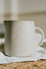 A white ceramic pitcher with a white handle sits on a white cloth. The pitcher is decorated with a pattern of dots, giving it a unique and artistic appearance. Concept of elegance and sophistication