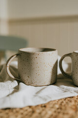A white coffee mug with a brown spot sits on a white cloth. The mug is placed on a table, and the cloth is spread out on the table. Concept of calm and relaxation, as the mug