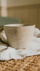 A white ceramic coffee cup with a brown rim sits on a white cloth. The cup is decorated with a pattern of dots, giving it a rustic and earthy feel. Concept of warmth and comfort