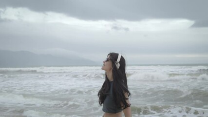 Young woman enjoying music on a cloudy beach walk along the shoreline