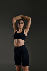 Fototapeta premium Sporty woman stretching in a stylish black outfit against a dark background
