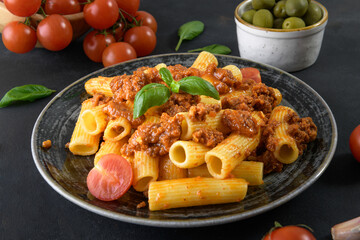 Traditional Italian rigatoni pasta with ragu sauce served on ceramic plate on dark table background