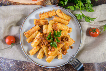Traditional italian rigatoni pasta with Bolognese sauce decorated with parsley on rustic style brown background, flat lay