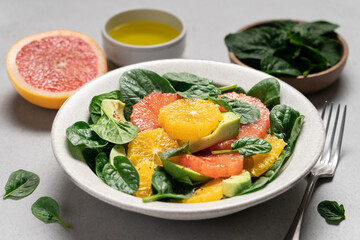 Fresh grapefruit avocado orange spinach salad in bowl. Healthy salad on gray background top view