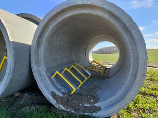 Large concrete pipes with metal barriers on grassy field under clear blue sky
